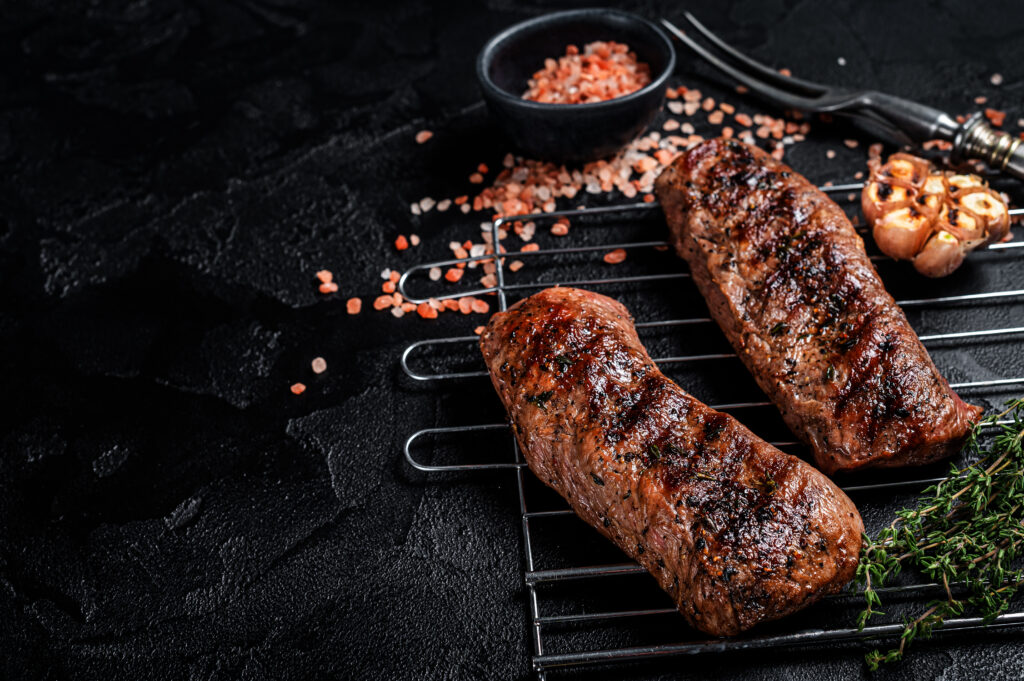 BBQ grilled Lamb tenderloin fillet meat on grill, mutton loin steak. Black background. Top view. Copy space.