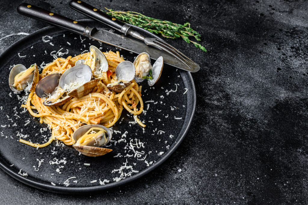 Seafood Spaghetti pasta with Clams vongole in a plate. Black background. Top view. Copy space.